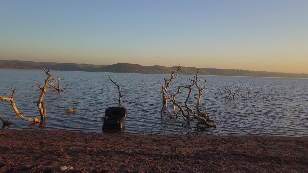 A chair in the ocean surrounded by branches during a sunset on a beach, orbit shot