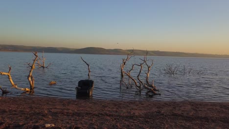 a chair in the ocean surrounded by branches during a sunset on a beach, orbit shot