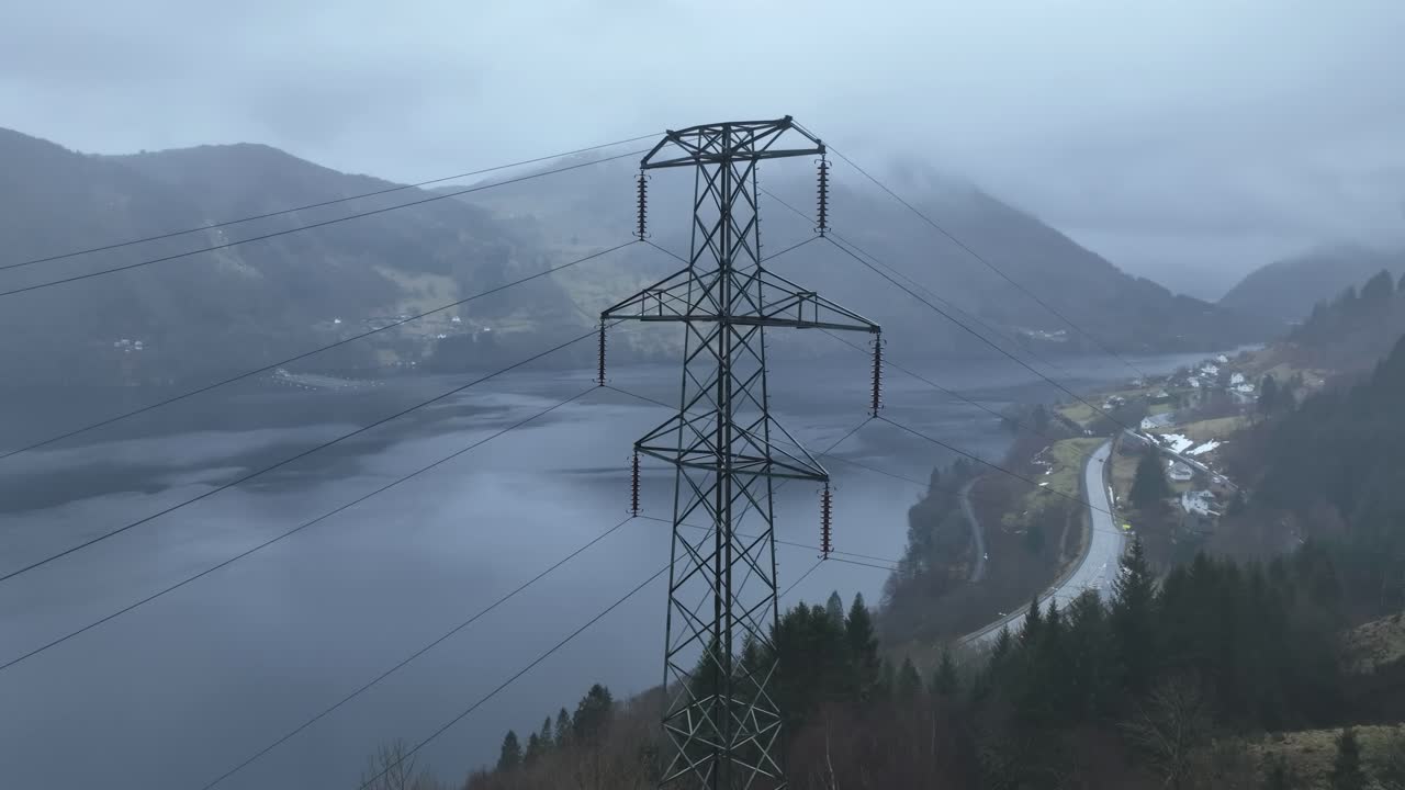 Approaching high voltage powerline mast in Bergen Norway, overlooking Sorfjorden and Osteroy. Main road E16 is visible below in a rainy, foggy atmosphere