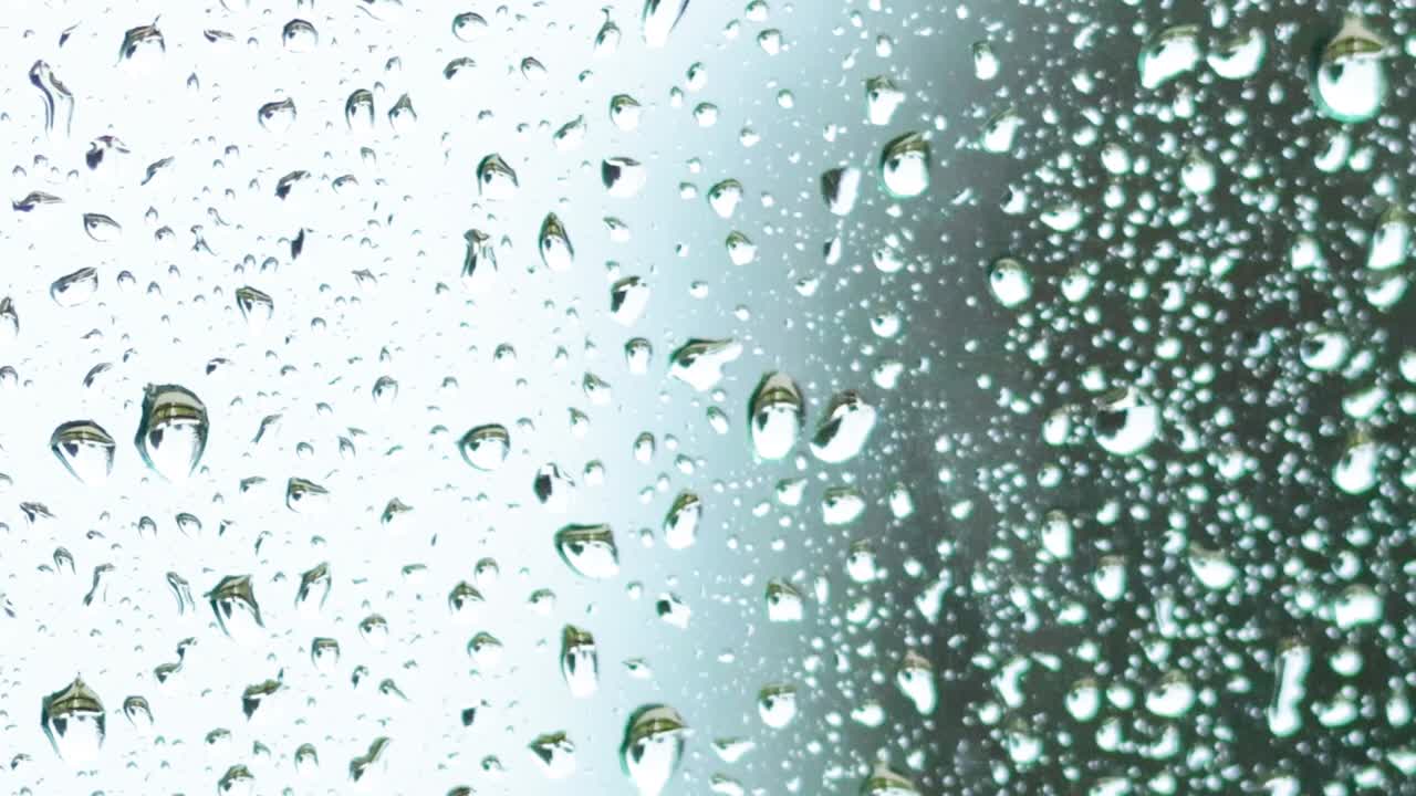 Primo piano dettagliato di gocce d'acqua che scivolano su una superficie di vetro trasparente durante un temporale