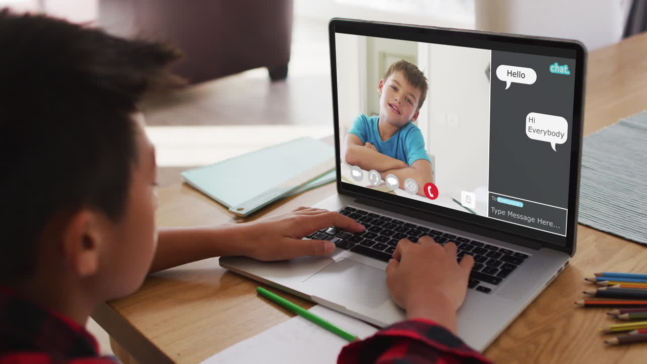 Schoolboy using laptop for online lesson at home, with school friend and web chat on screen