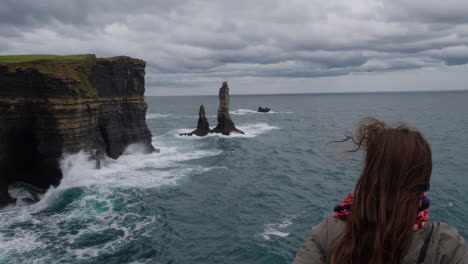 person overlooking the dramatic cliffs of moher and sea stacks on a windy day