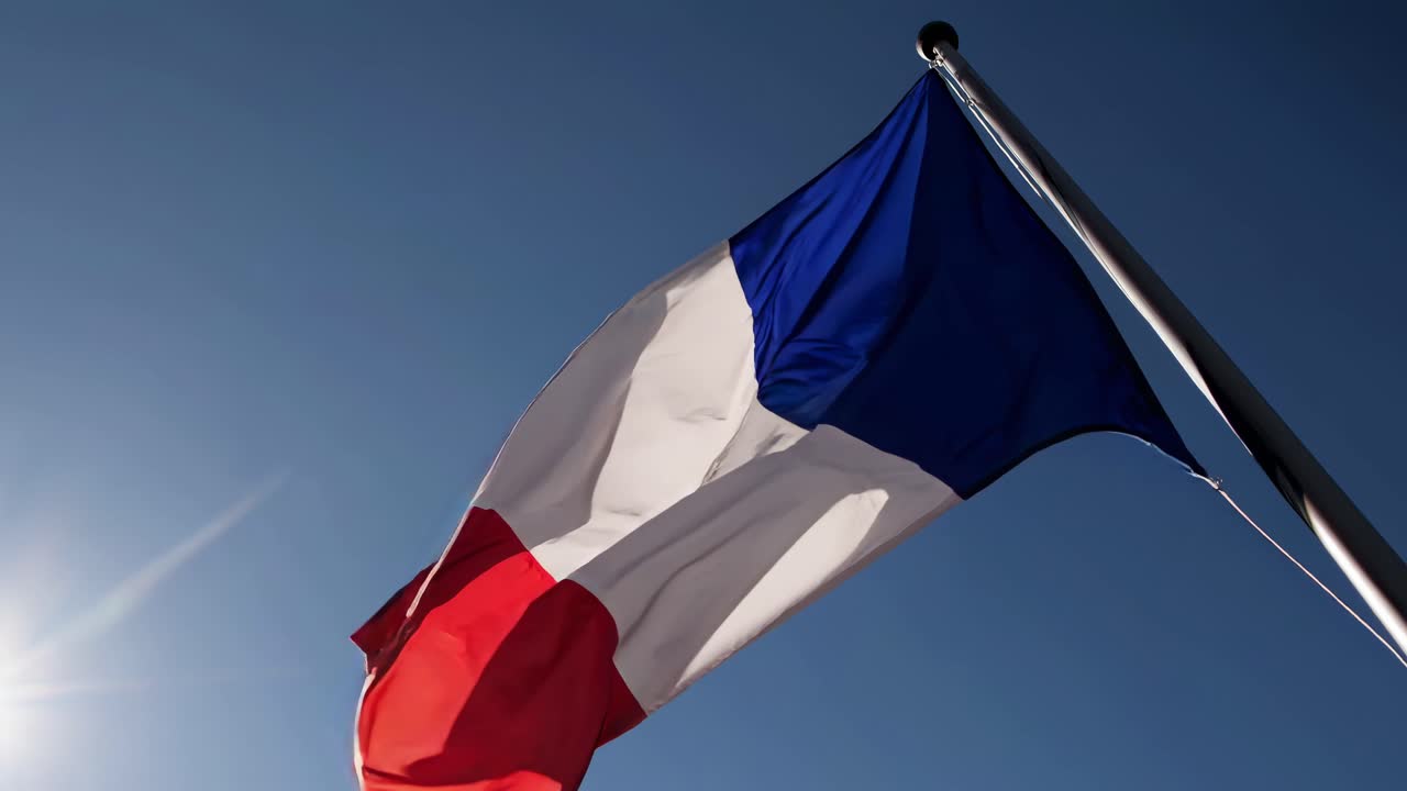 Low-angle video shot of a French flag waving against a clear blue sky, capturing the vibrant colors