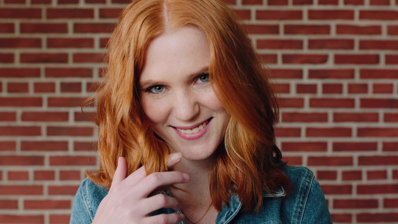 Young Woman with Red Hair Smiling and Playing with Her Hair