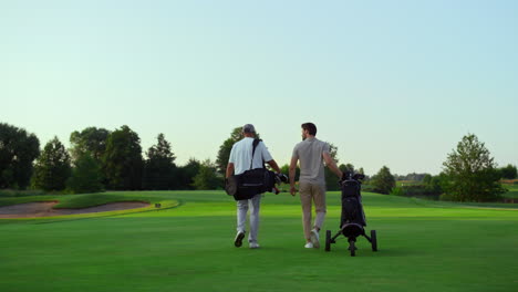 Rich-golf-players-walking-on-field.-Two-active-sportsmen-carry-equipment-clubs.