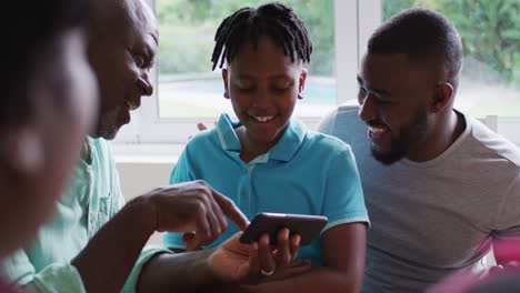 African-american-grandfather,-father-and-son-smiling-while-using-smartphone-together-at-home