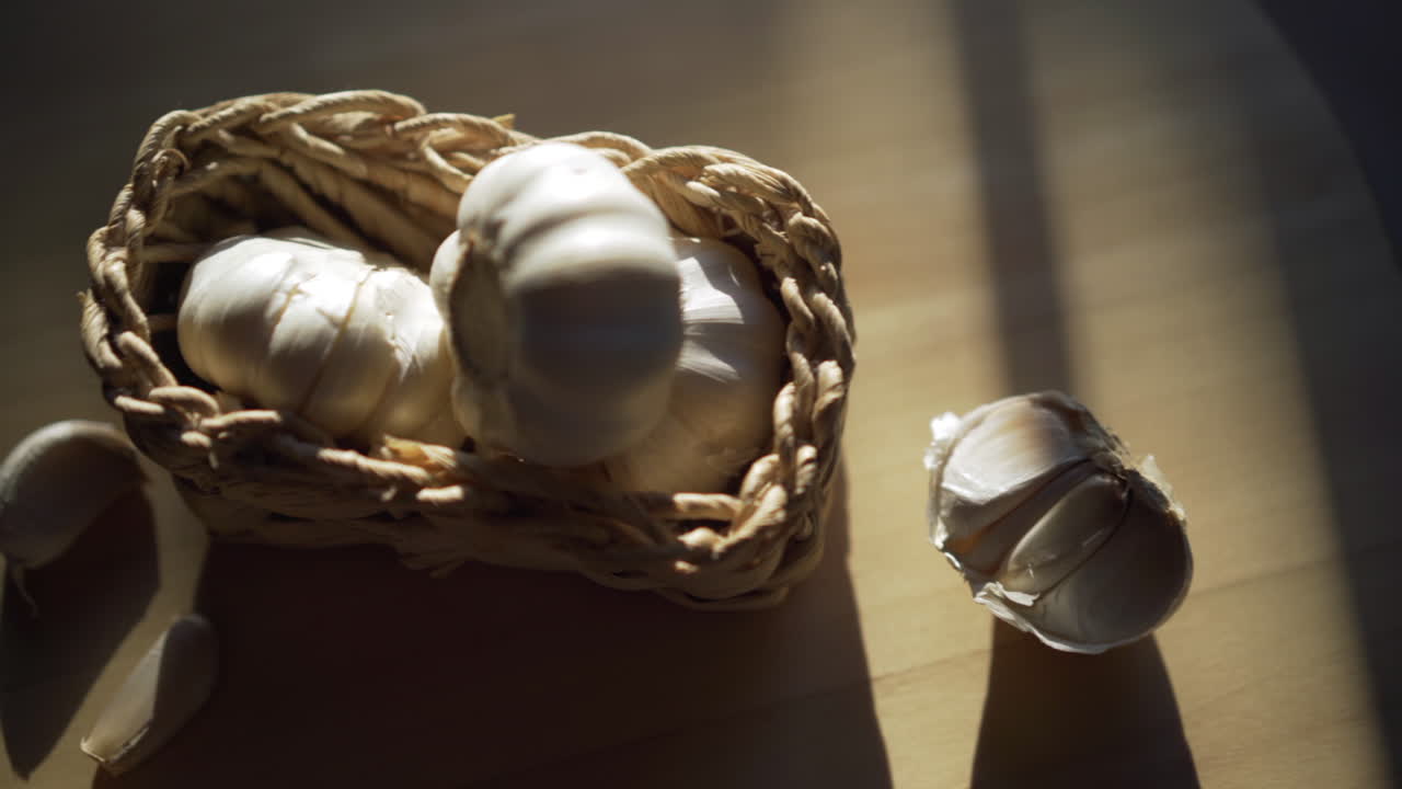 ajo en una cesta sobre una mesa de madera algunos dientes separados, sol creando sombras sobre la mesa