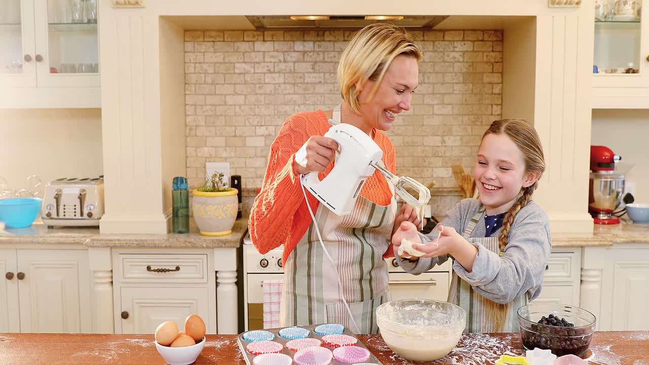 Smiling mother holding whisk while daughter playing with mixture 4K 4k