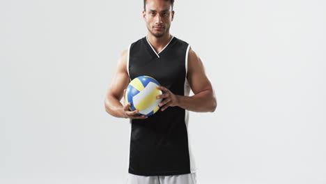 young biracial man holding a volleyball on a white background, with copy space