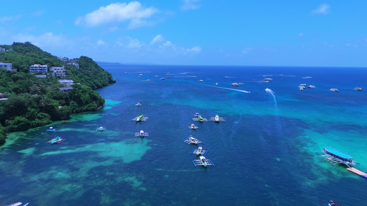 4K drone footage of traditional boats floating in vivid blue water near lush Boracay cliffs—ideal for travel, island culture, or cinematic ocean scenes