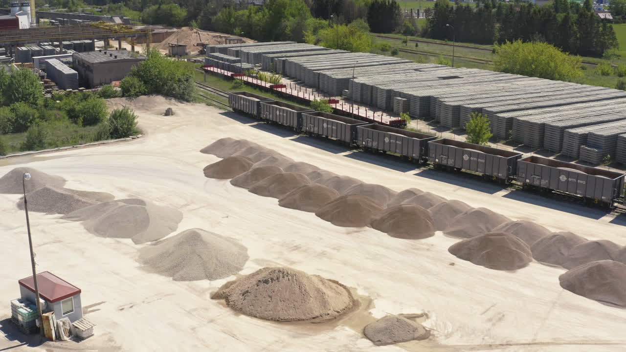 Open Storage Yard With Rows Of Sand And Gravel Piles For Loading Into Railcars, Stacks Of Concrete Slabs In Background. aerial shot