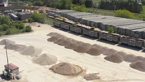 open storage yard with rows of sand and gravel piles for loading into railcars, stacks of concrete slabs in background. aerial shot