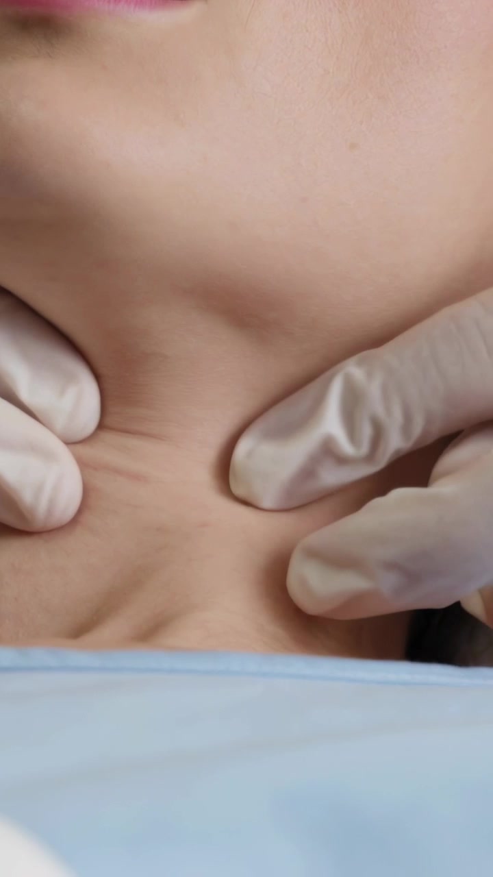 Video verticale: Mani guantate che palpano il collo in clinica, controllando la mobilità, con un camice blu.