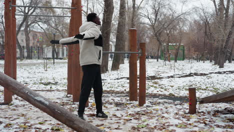 young boy outdoors performing arm stretches in winter. snow covers ground, surrounded by workout equipment, and trees in background