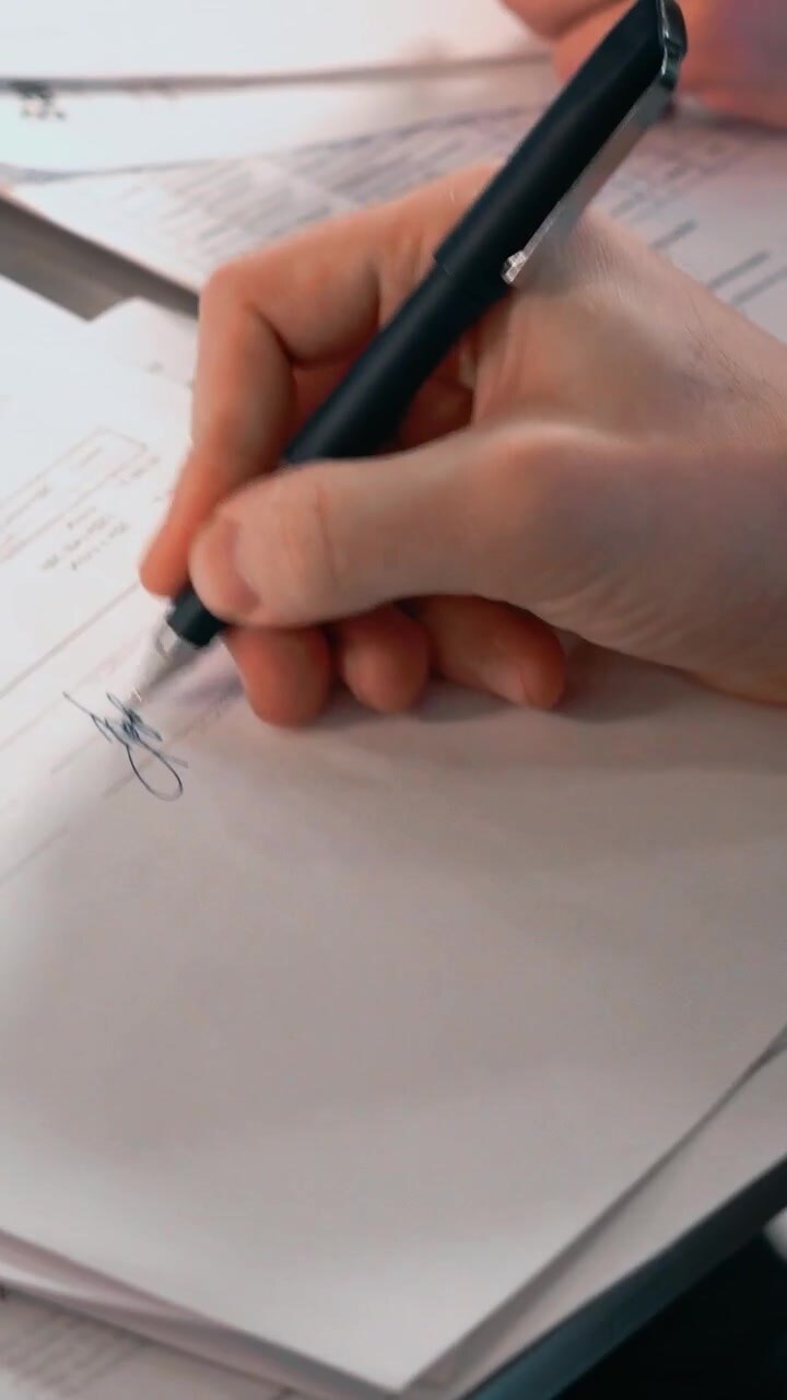 Close up of hands signing documents with a pen over papers
