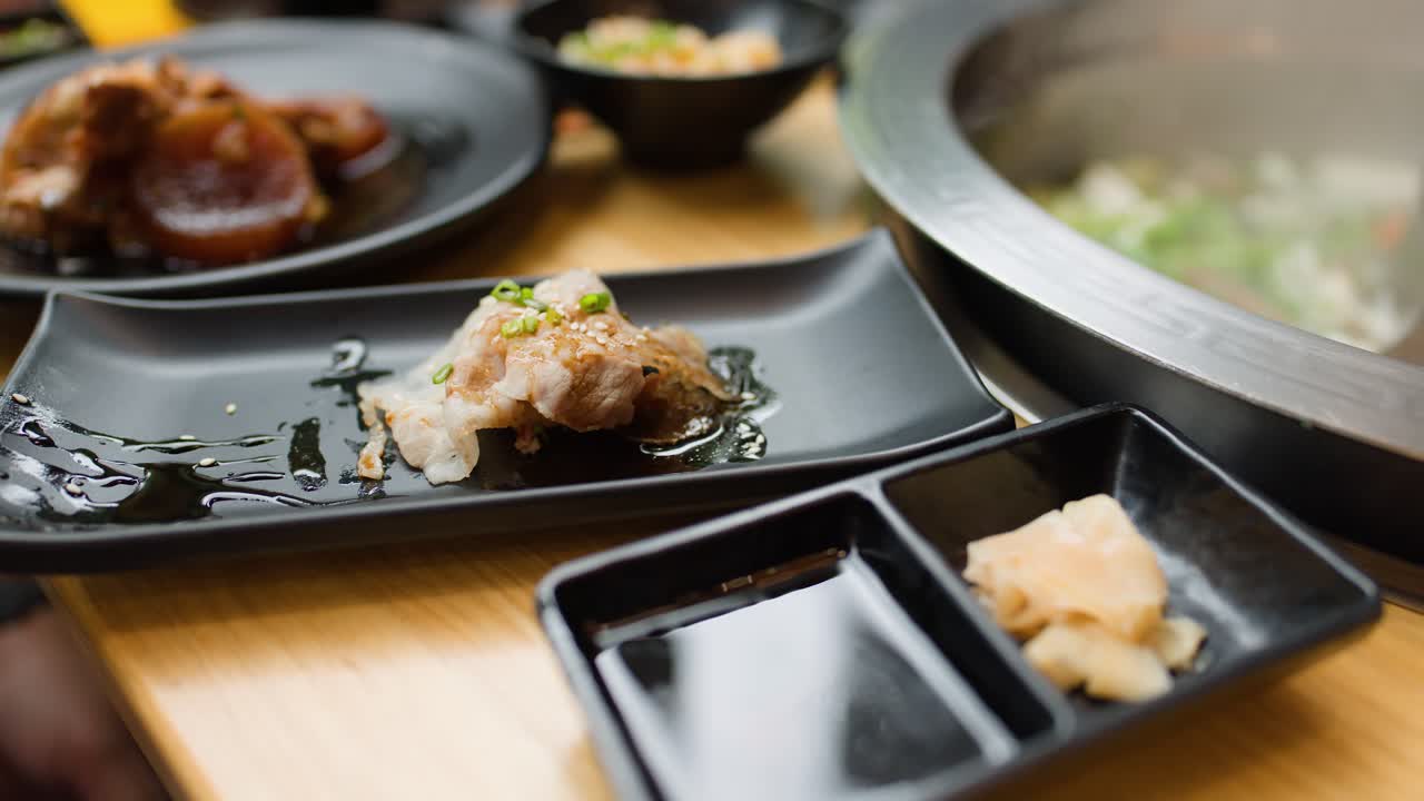 Chopsticks pick up cooked shabu meat from plate, dipping into soy sauce, bright restaurant lighting