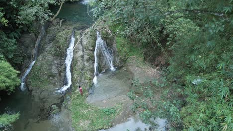 Aufsteigende-Luftaufnahme-Einer-Frau,-Die-In-Zeitlupe-An-Einem-Kaskadierenden-Wasserfall-Auf-Der-Karibischen-Insel-Tobago-Steht