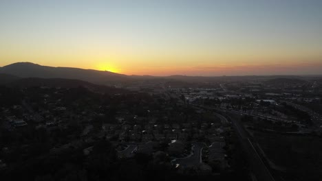 El-Dron-Captura-Una-Impresionante-Toma-Aérea-De-La-Puesta-De-Sol-En-La-Pequeña-Ciudad,-Elevándose-Cada-Vez-Más-A-Medida-Que-Los-Colores-Del-Cielo-Cambian-Y-La-Luz-Del-Atardecer-Alcanza-El-Horizonte.