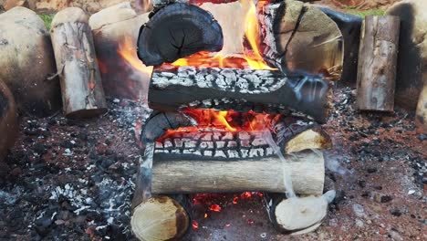 logs stacked in a log-cabin style in a fire pit while flames burn the wood