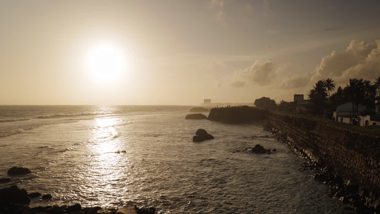 Sunset view over sea with slow flowing golden ocean and silhouetted people on Galle fort, Sri Lanka.