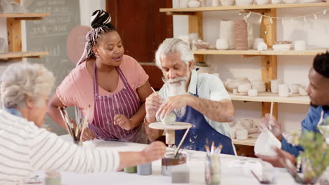 Happy-diverse-group-of-potters-glazing-clay-jugs-and-discussing-in-pottery-studio