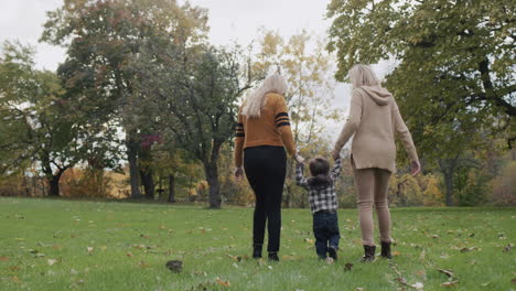 Two-young-women-walking-with-a-toddler-in-the-park,-having-a-good-time-together