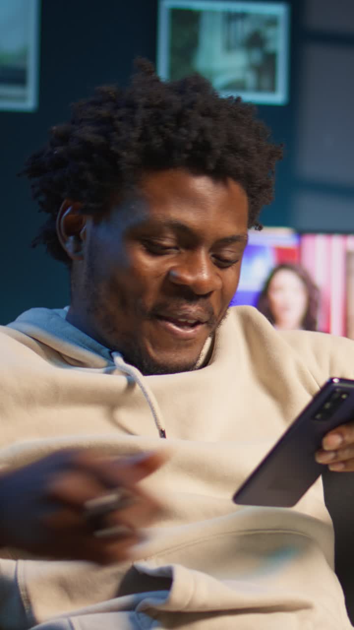 Giovane uomo afroamericano che si rilassa sul divano con smartphone e caffè