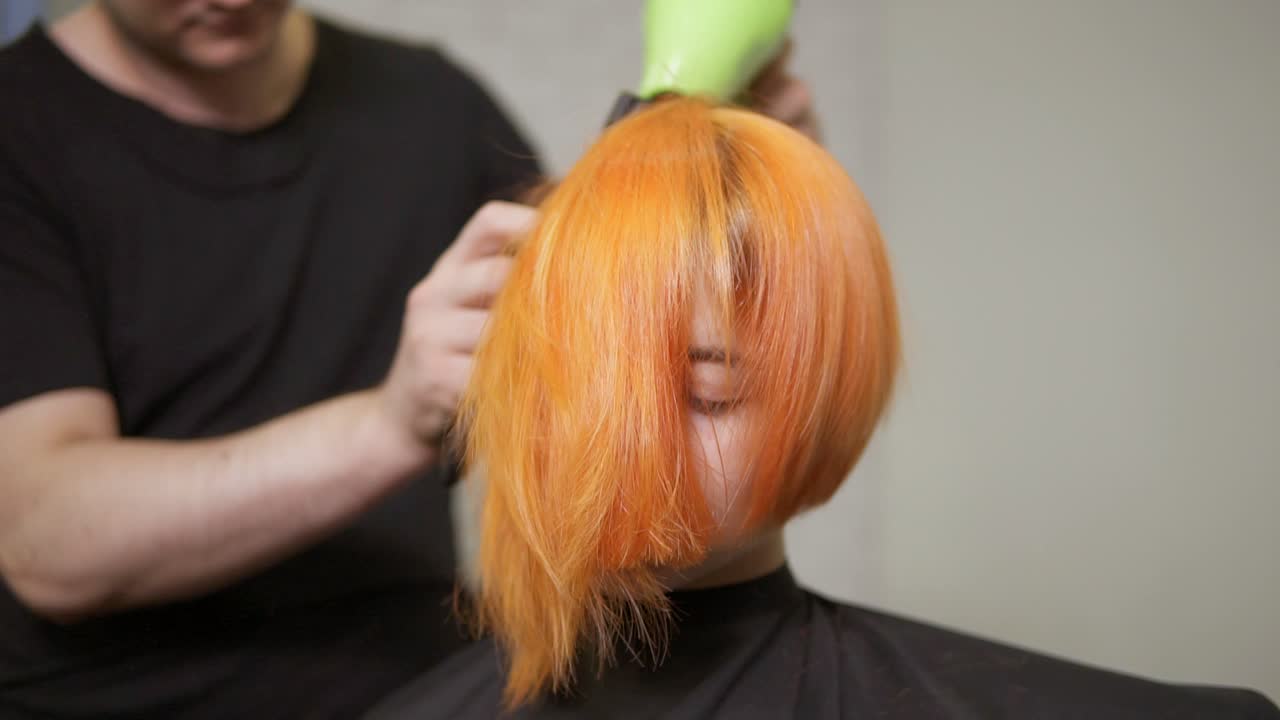 머리카락을 자른 후 헤어 드라이어를 사용하는 전문 미용사. 미용실에서 젊은  ⁇ 은 머리 여성. 느린 동작 촬영