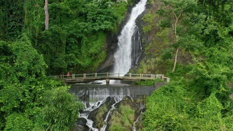 aerial zoom out of girl walking across a bridge at kerta gangga waterfall in lombok