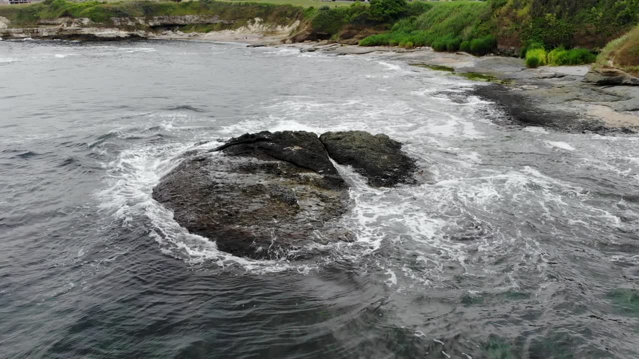 흐린 날에 해안에 가까운 바다에서 평평한 바위 주위에 공중 팬 샷