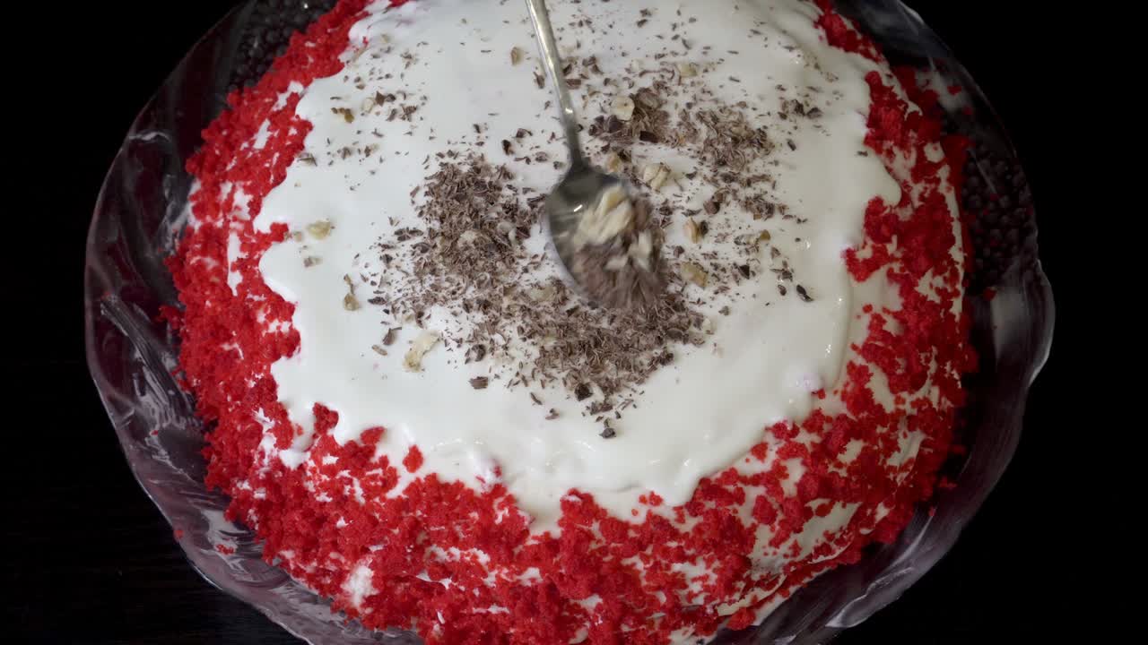 한 여성이 은 견과류, 초콜릿 및 은 크림으로 아름다운 생일 케이크를 장식합니다. 검은 테이블에 은 케이크. 격리 기간 동안 집에서 소규모 사업. 근접. 상단 뷰. 얼굴없는. 4k.