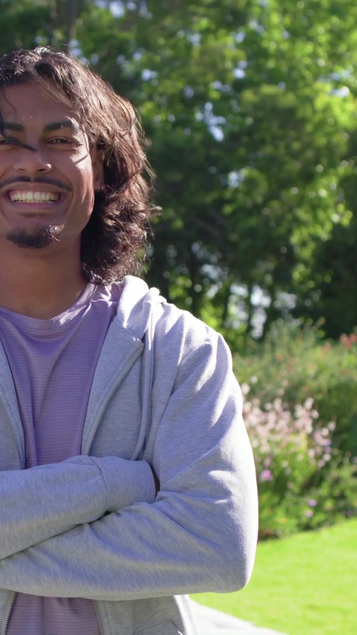 Vertical video: Smiling man arms crossed in yard, zooming out showing hoodie and Tshirt, copy space