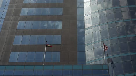 modern glass skyscraper with ecuadorian and malaysian flags swaying in the wind