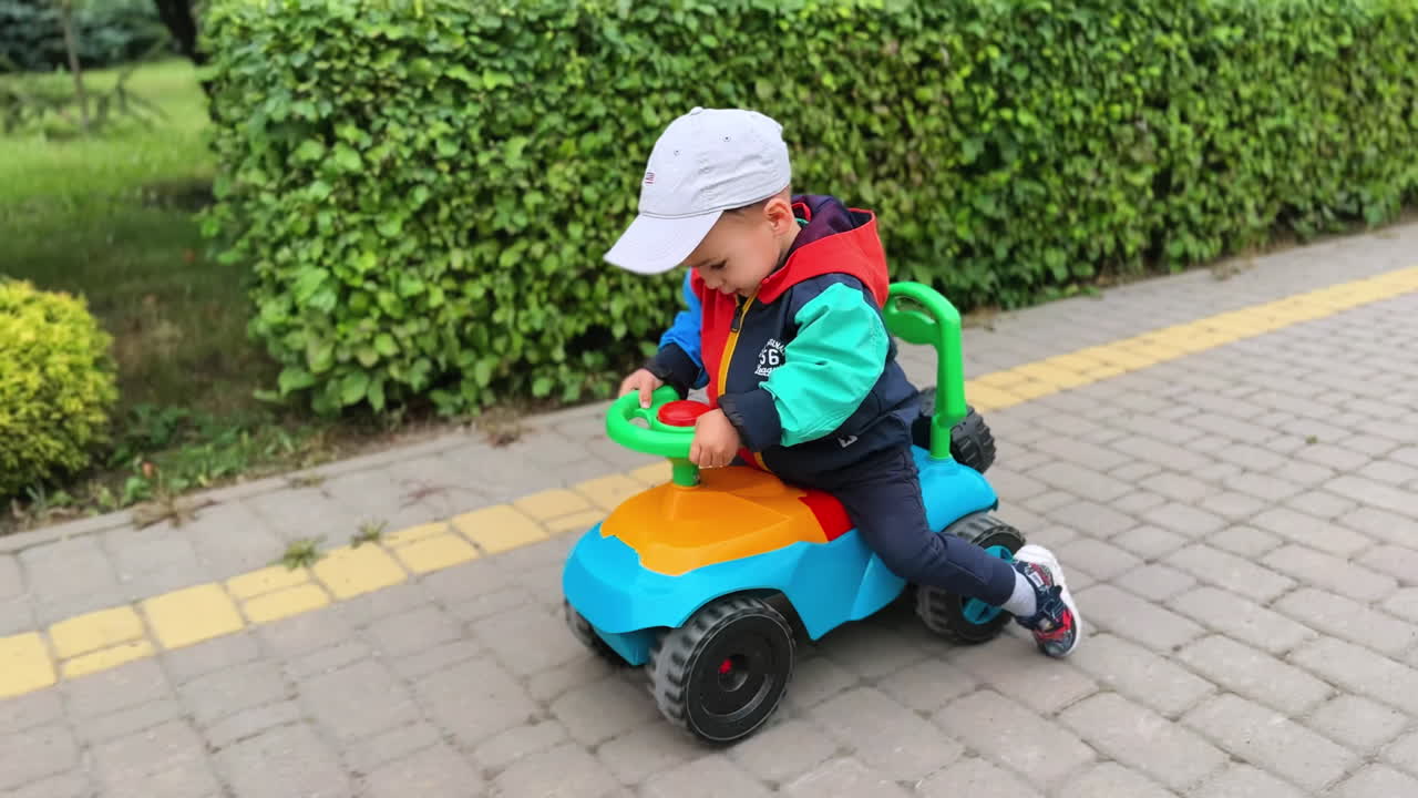 Beautiful smiling toddler boy in a cap sitting on the toy car. Kid riding quickly pushing from the ground.