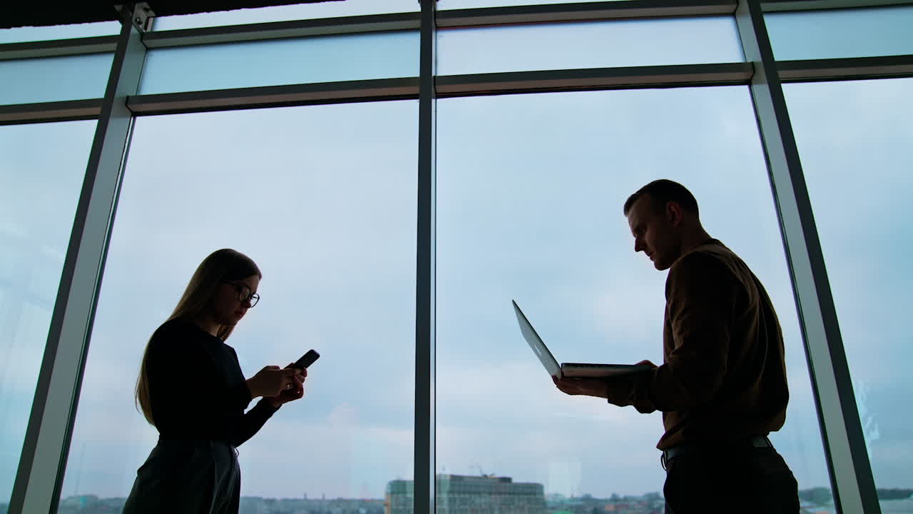 Young workers use laptop and phone in office. Business people changing their gadgets on the sky background through the windows. Business concept.