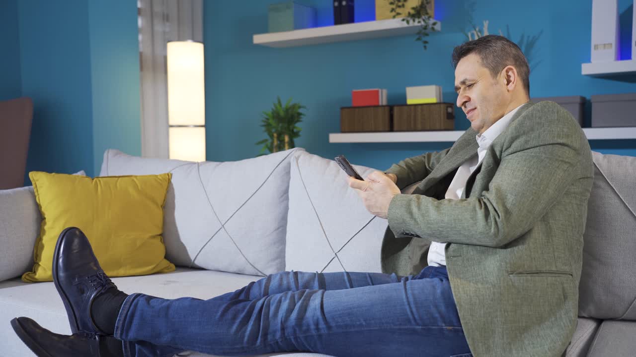 거실의 소파에서 휴식을 취하는 동안 스마트 폰을 사용하는 흥분 된 남자.