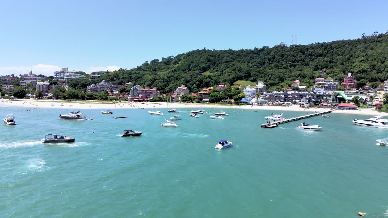 플로리아노폴리스 브라질 관광 해변의 공중 드론 장면, 부두와 바다에 많은 보트와 쾌속정, 바다를 마주한 많은 집들이 있는 해변 옆에서 항해하는 많은 사람들