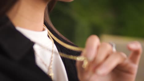 close up shot of a young caucasian woman touching her golden necklace jewellery wearing silver rings stiting on a bench feeling nostalgic relaxing by herself isolated blurry backround slow motion