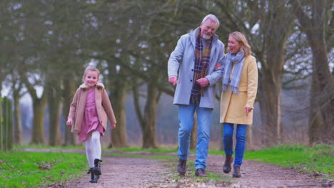grandparents watching granddaughter skipping ahead on outside walking through winter countryside