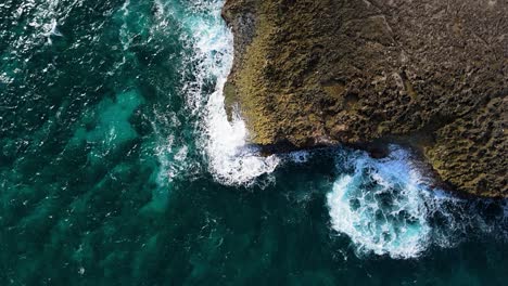 el avión no tripulado asciende y gira a medida que las olas del océano golpean la escarpada costa volcánica de la isla.