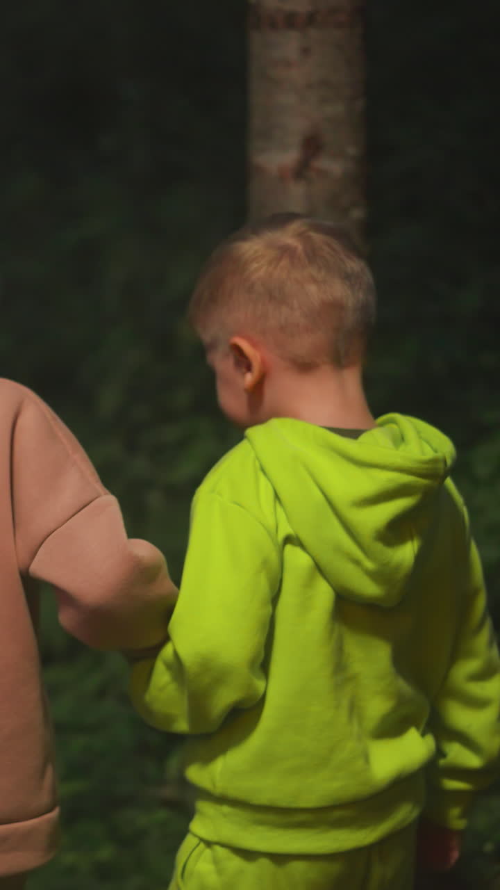 los niños pequeños caminan juntos por el bosque nocturno. un hermano y una hermana curiosos se dan la mano caminando por el parque salvaje por la noche. niños felices de vacaciones