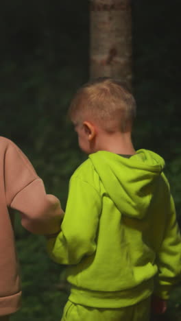 los niños pequeños caminan juntos por el bosque nocturno. un hermano y una hermana curiosos se dan la mano caminando por el parque salvaje por la noche. niños felices de vacaciones