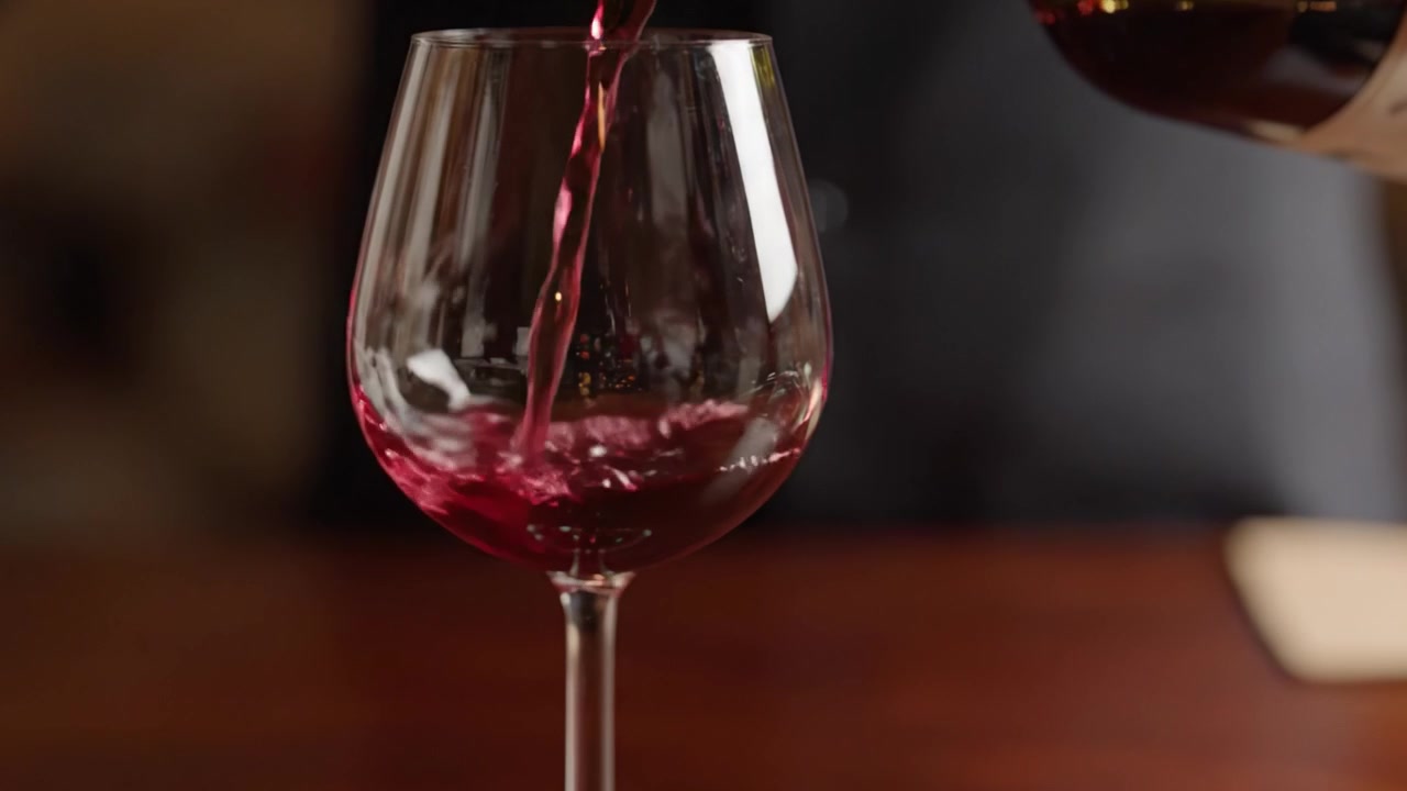 Una mescita perfetta: L'arte del vino versato in un bicchiere che mostra colori ricchi e la superficie riflettente del vetro in un'atmosfera accogliente