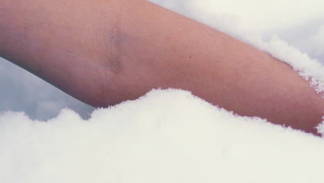 mature woman puts bare hand with manicure into white snow