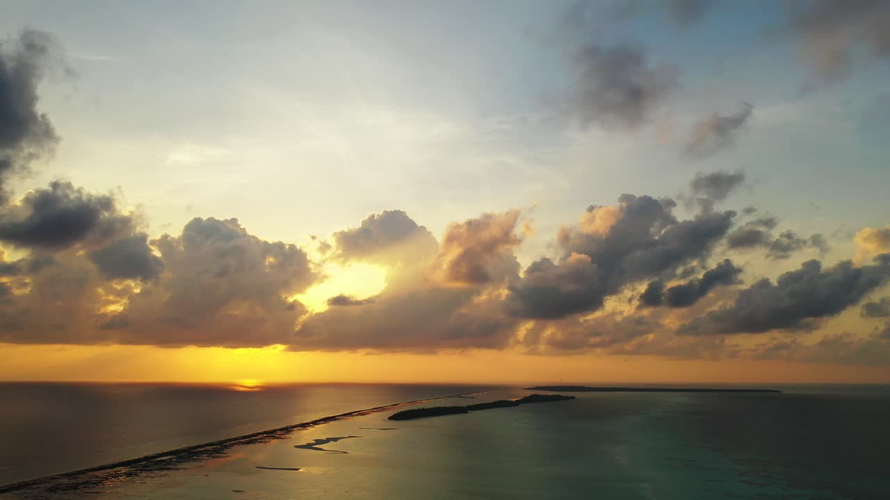 Beautiful sunset with grey clouds hiding yellow sun shining on bright sky reflecting over dark surface of endless ocean in Maldives