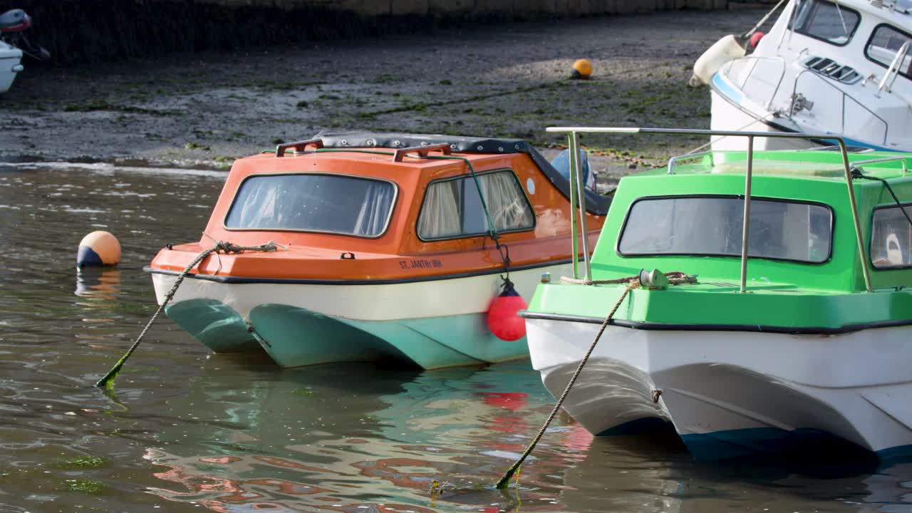 Two colorful motorboats gently bob on calm harbor water under natural daylight, static camera view