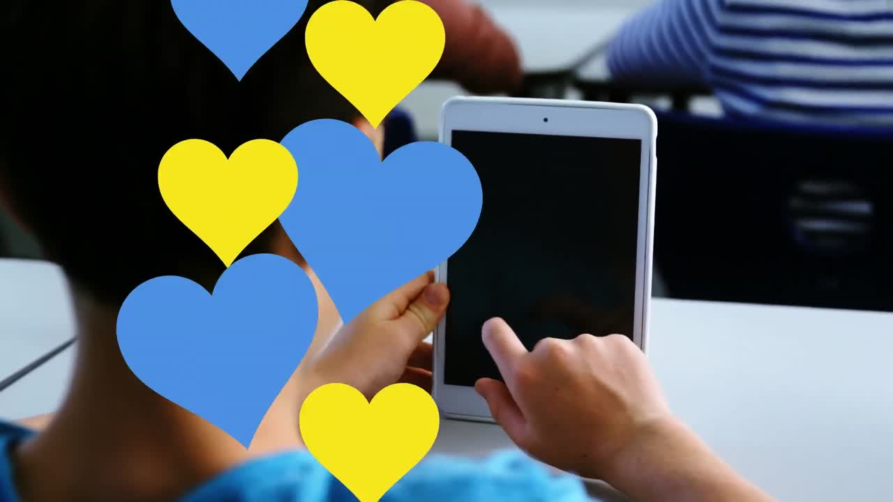 학교에서 디지털 태블릿을 사용하는 백인 소년의 뒷면에 여러 개의 파란색과 빨간색 심장 아이콘이 있습니다.