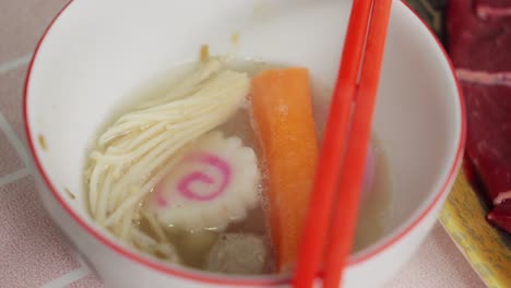 Bowl-Of-Kagosei-Narutomaki,-Enoki-Mushroom-And-Crab-Stick-Boiled-In-Hot-Water-Steaming,-Close-Up