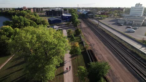 Two-cyclists-on-urban-bike-parkway-path-along-bus-and-train-line,-public-transportation-and-commuting