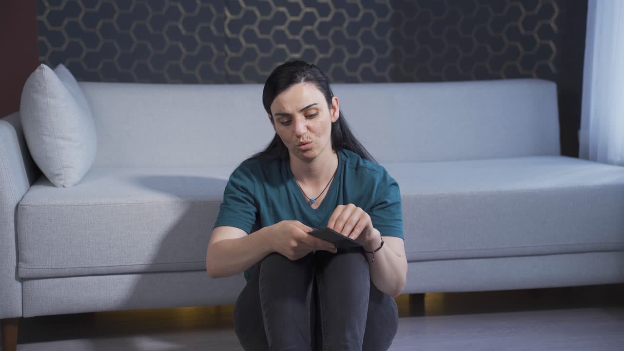 la mujer sentada junto a la pared mira su billetera vacía. quebrada.
